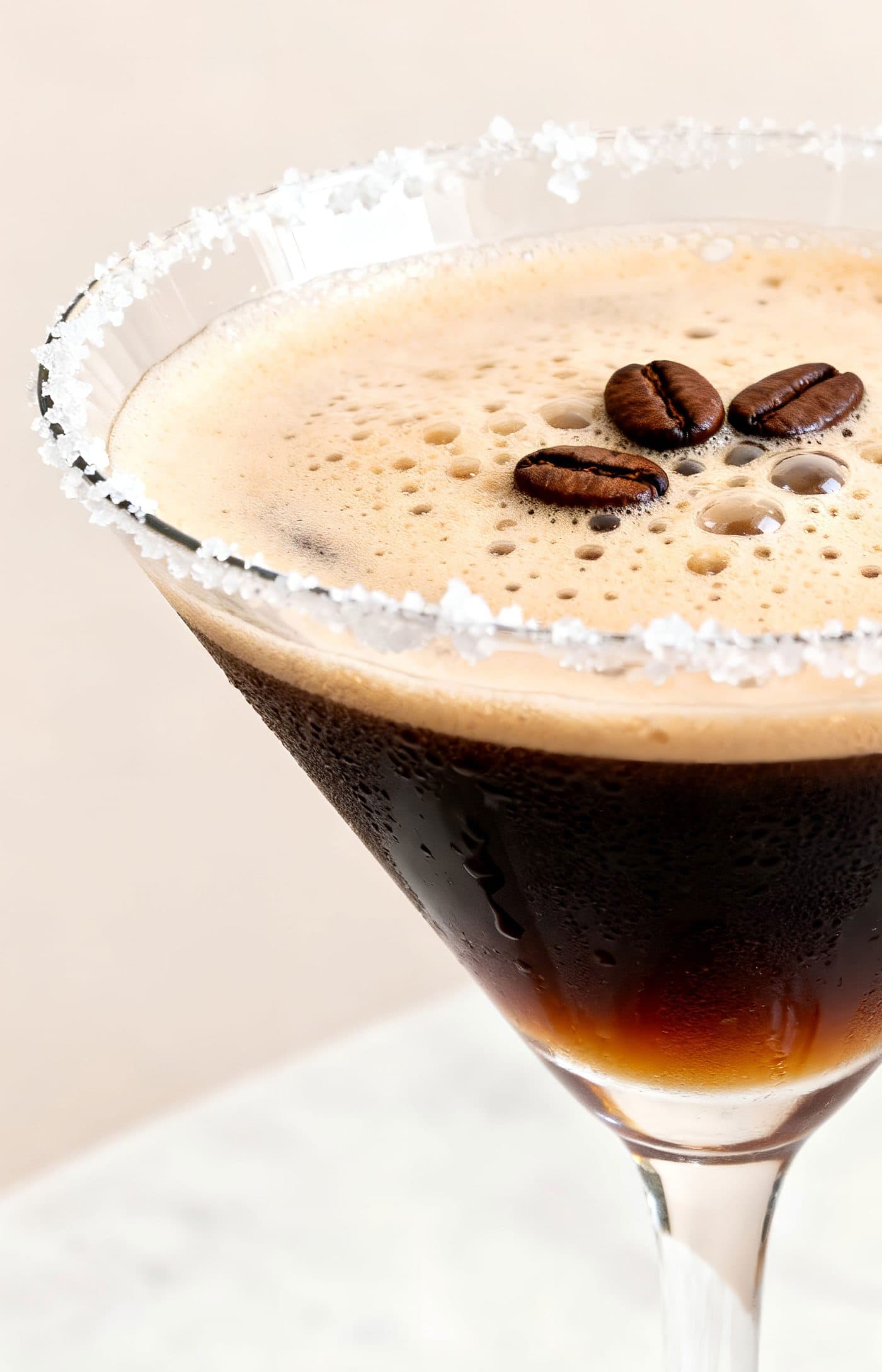An espresso martini with a salted rim and three coffee beans on the crema