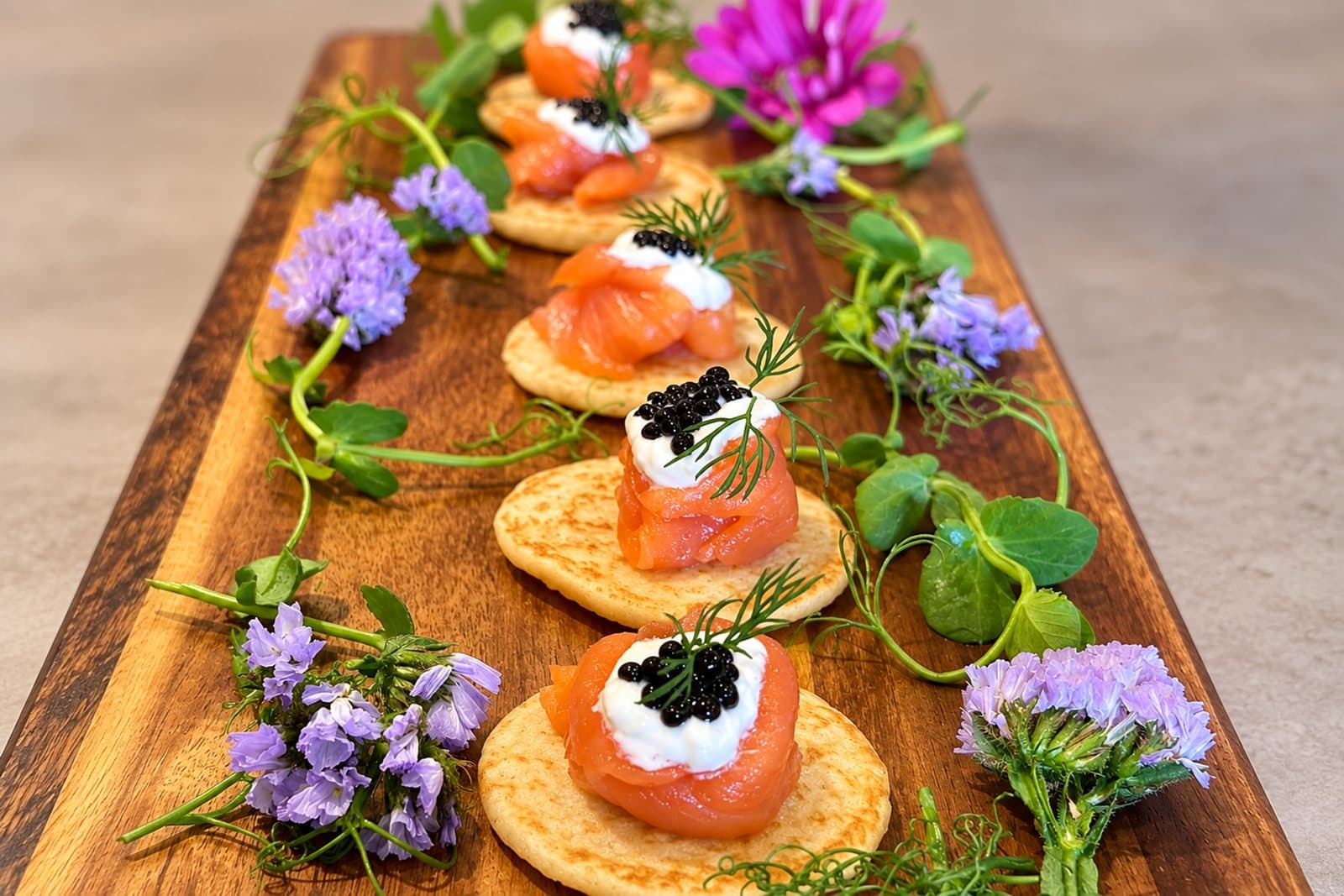Smoked salmon blinis with crème fraîche and caviar on a wooden board with edible flowers