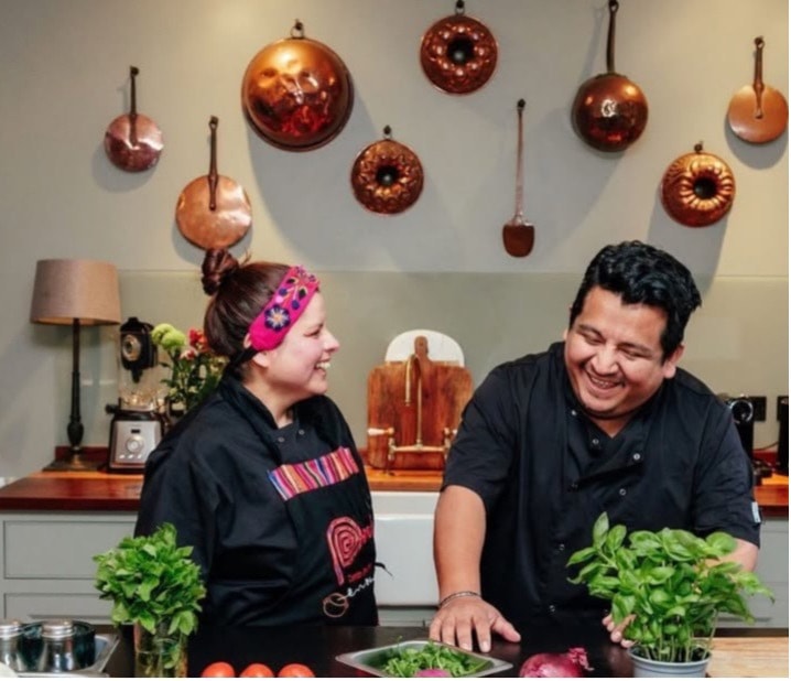 The Judith's Kitchen team laughing together in the kitchen, fresh herbs on the counter in front of them