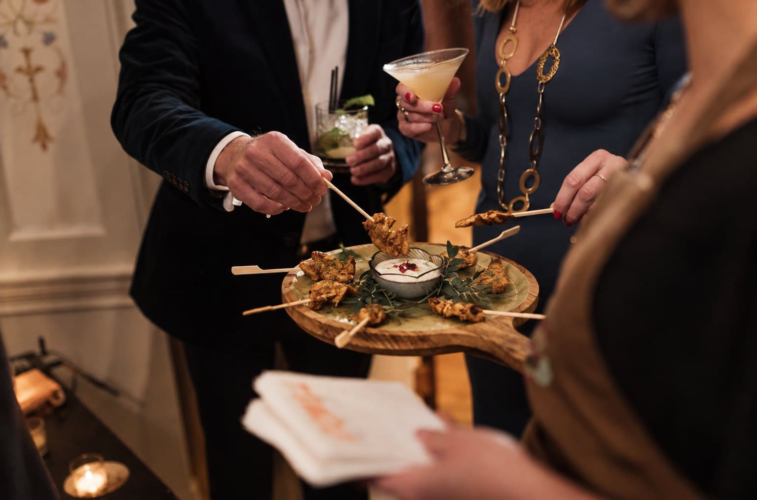 Guests in evening dress taking canapés from a wooden board at a drinks reception